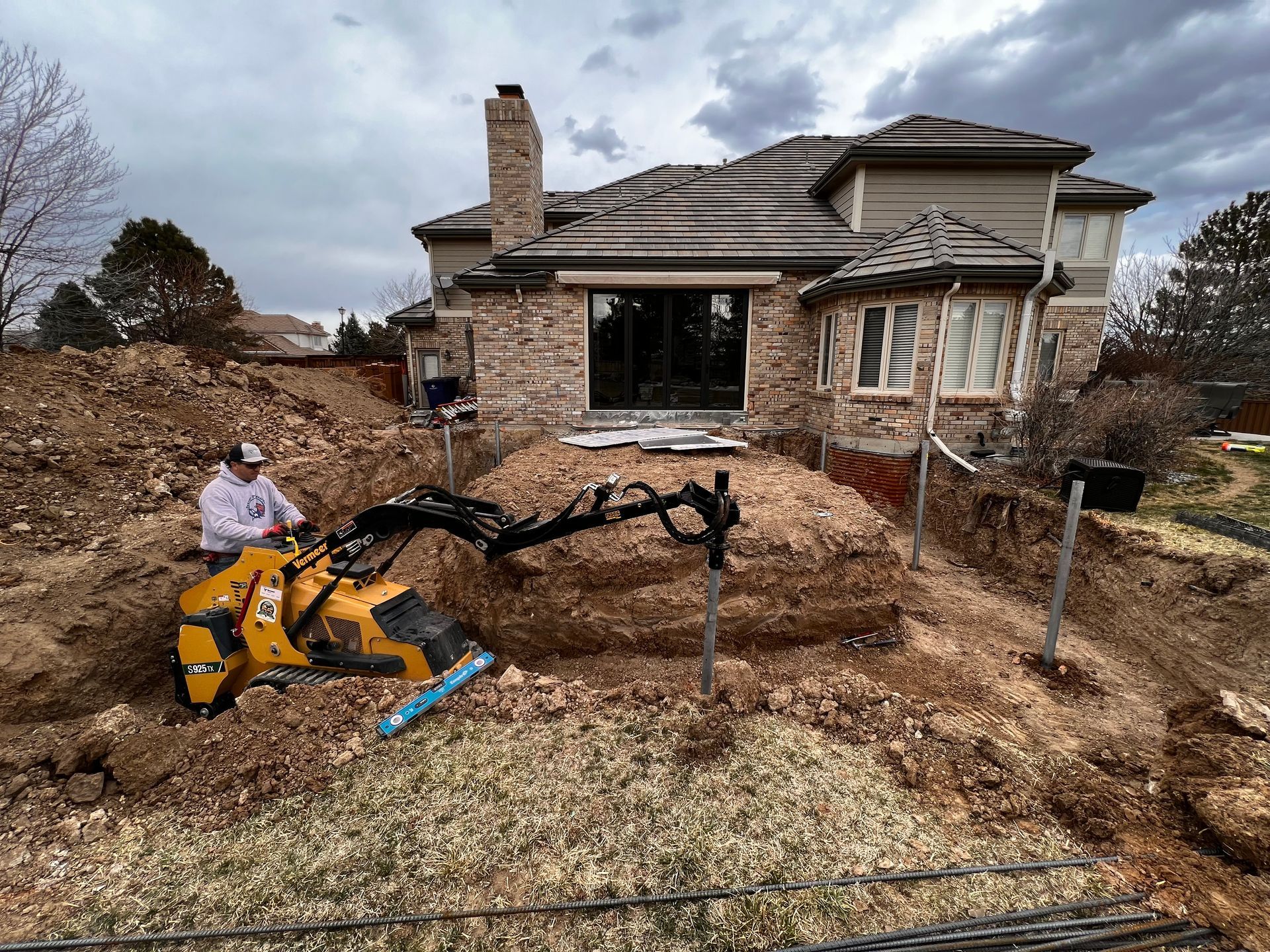 A man is digging a hole in the dirt in front of a house.