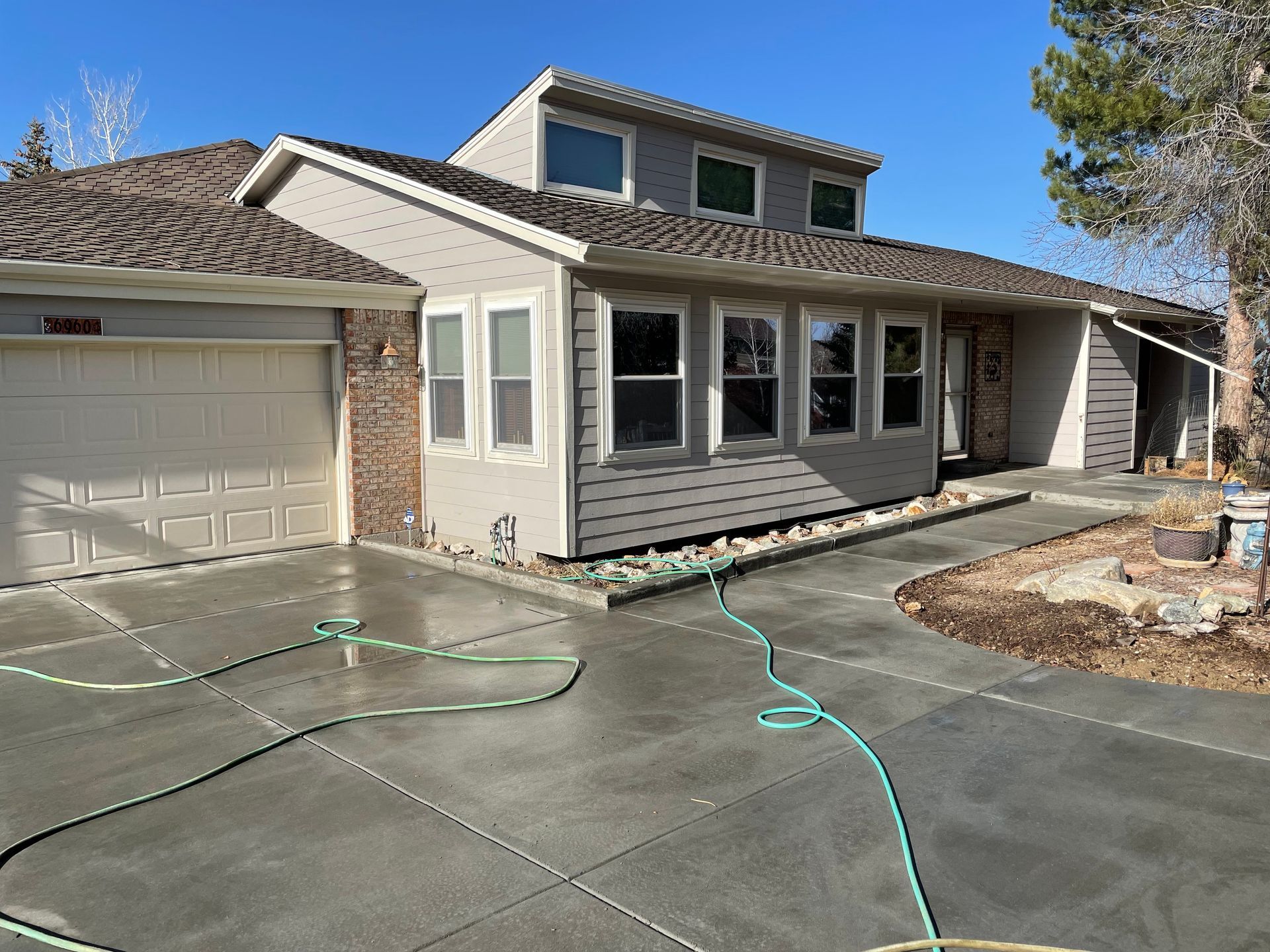 A house with a hose in front of it and a concrete driveway.