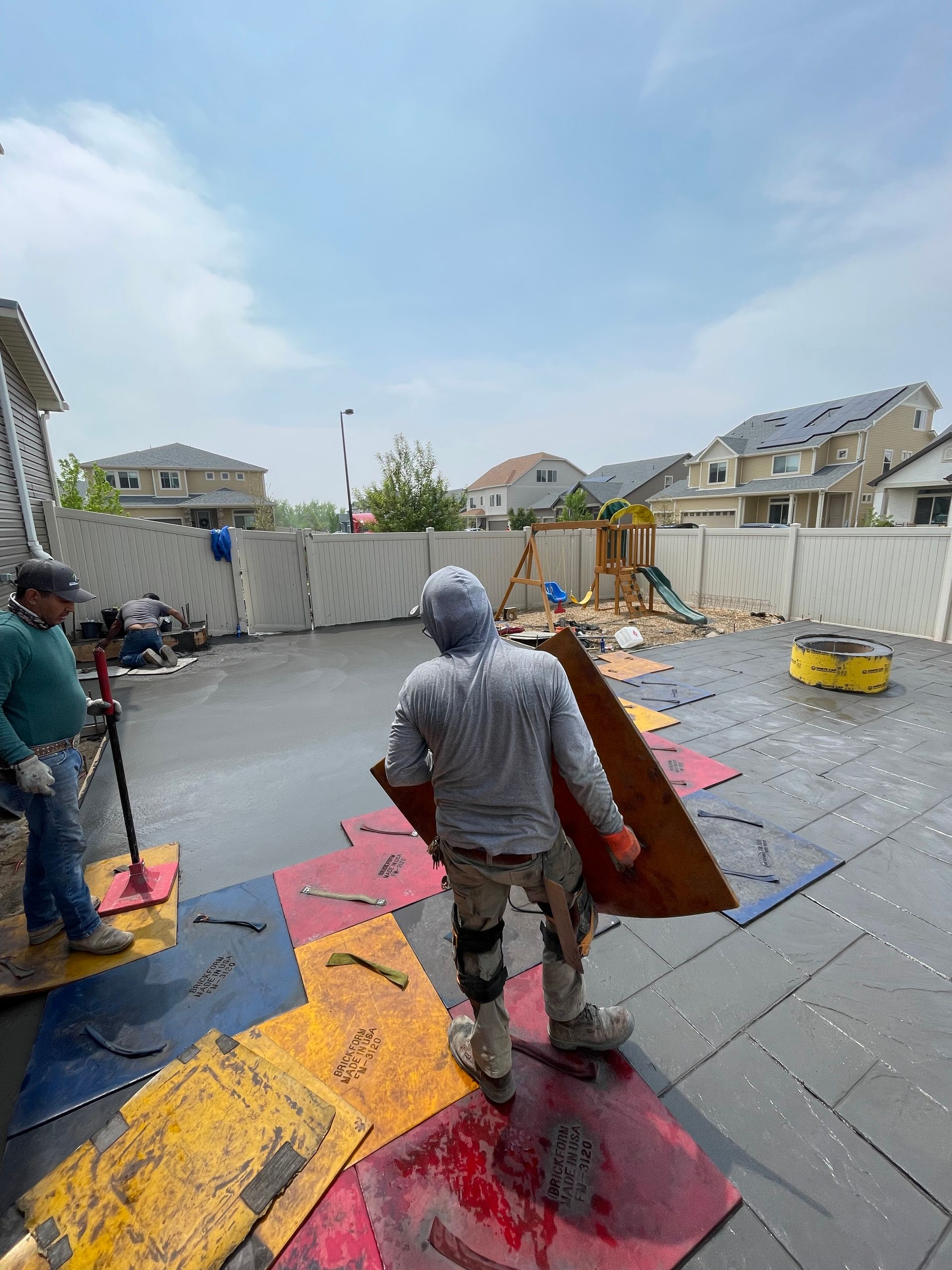 A man is carrying a piece of wood in a backyard.