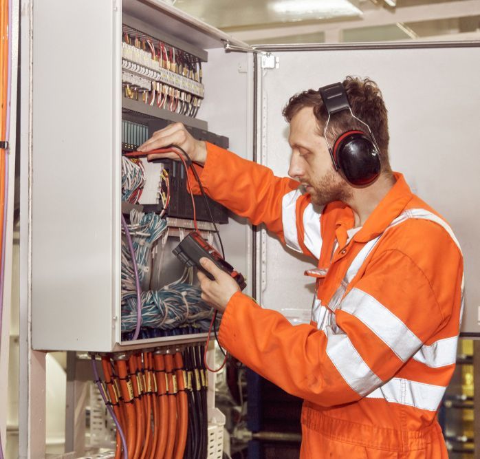 A Man Wearing Headphones Is Working On An Electrical Box — Steve Mason Electrical In Port Macquarie, NSW