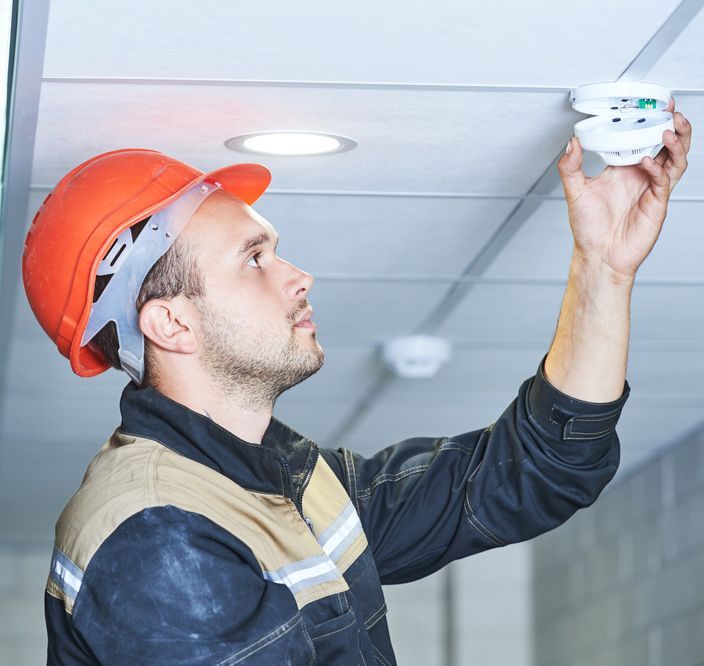 A Man Wearing An Orange Hard Hat Is Installing A Smoke Detector — Steve Mason Electrical In Port Macquarie, NSW