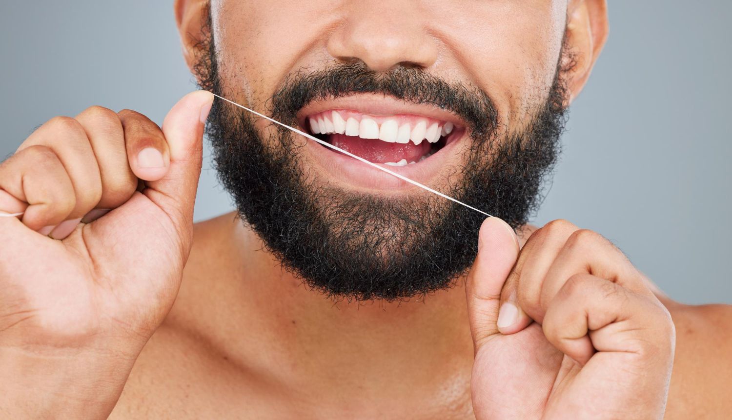 A man with a beard is flossing his teeth.