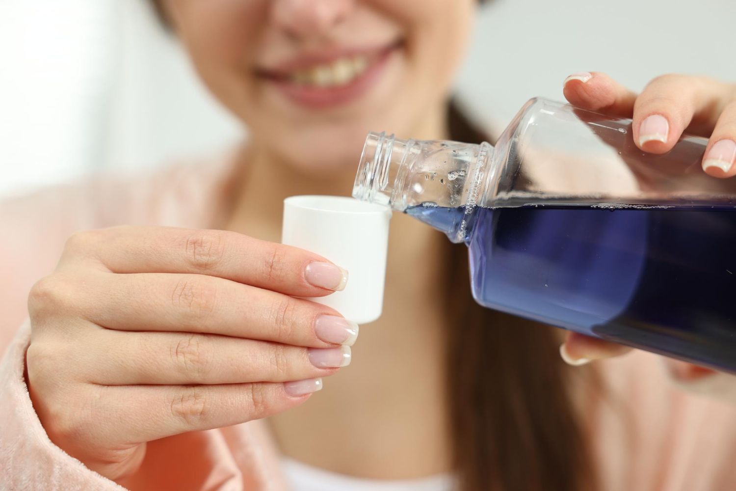 A woman is pouring mouthwash into a measuring cup.