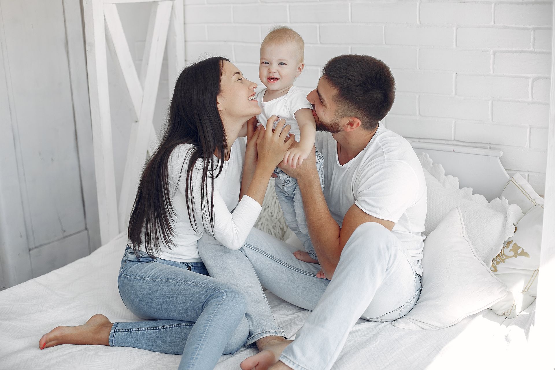 A man and a woman are sitting on a bed holding a baby.
