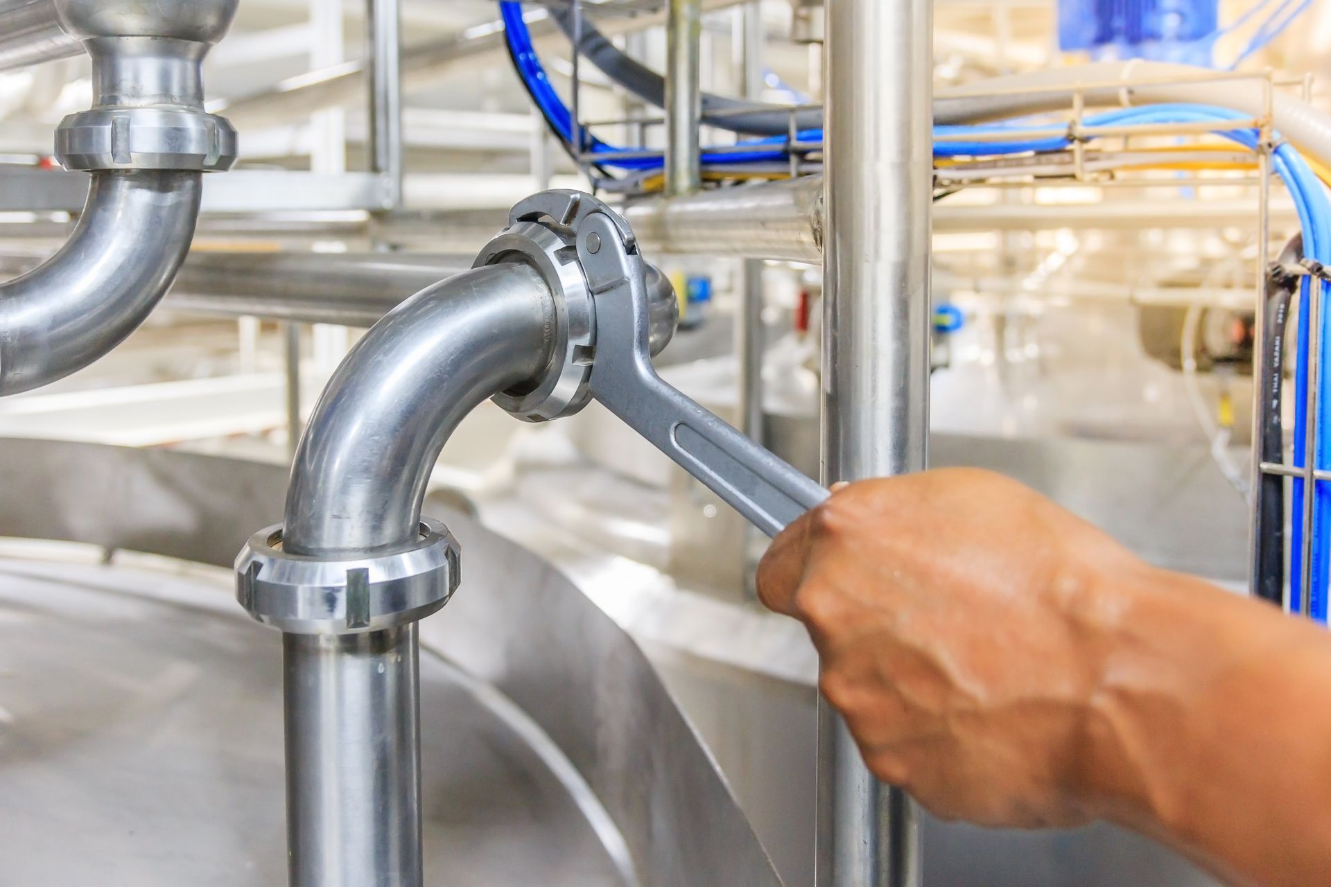 A person is fixing a pipe with a wrench in a factory.