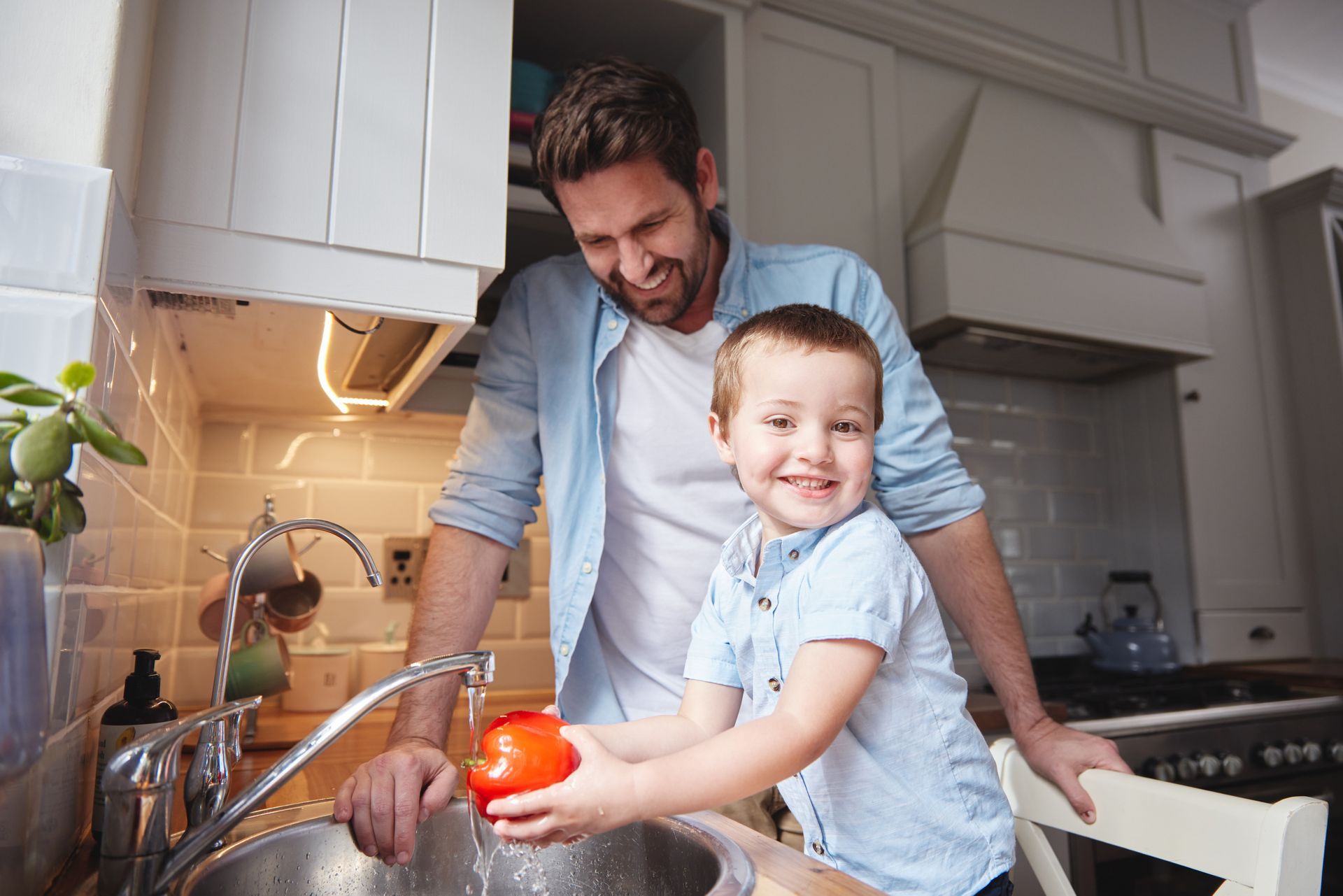 A man and a boy are washing tomatoes in a kitchen sink.