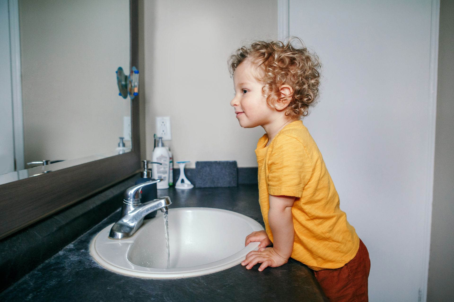 A woman and a little girl are washing dishes in a kitchen sink.