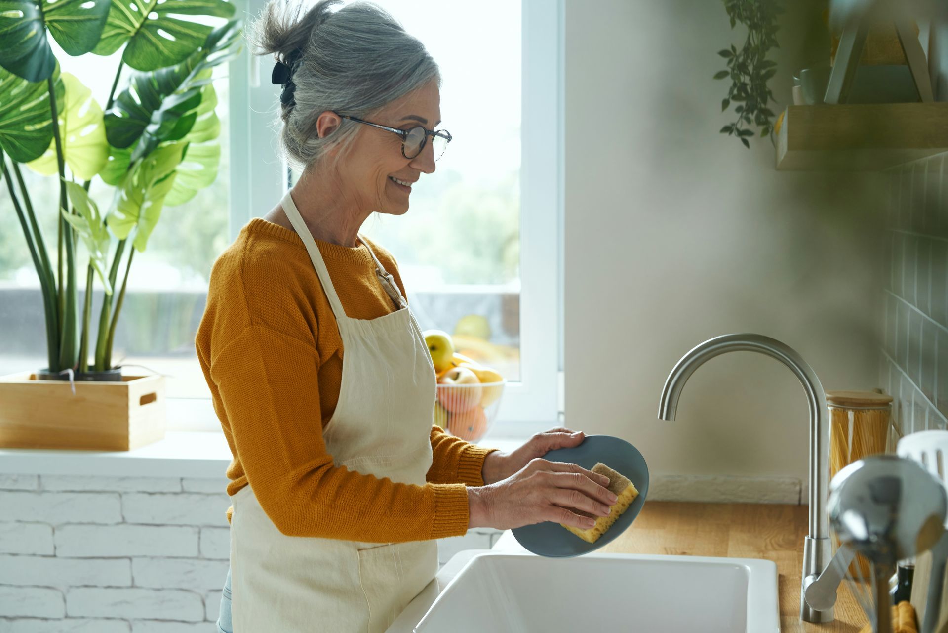 A woman and a little girl are washing dishes in a kitchen sink.