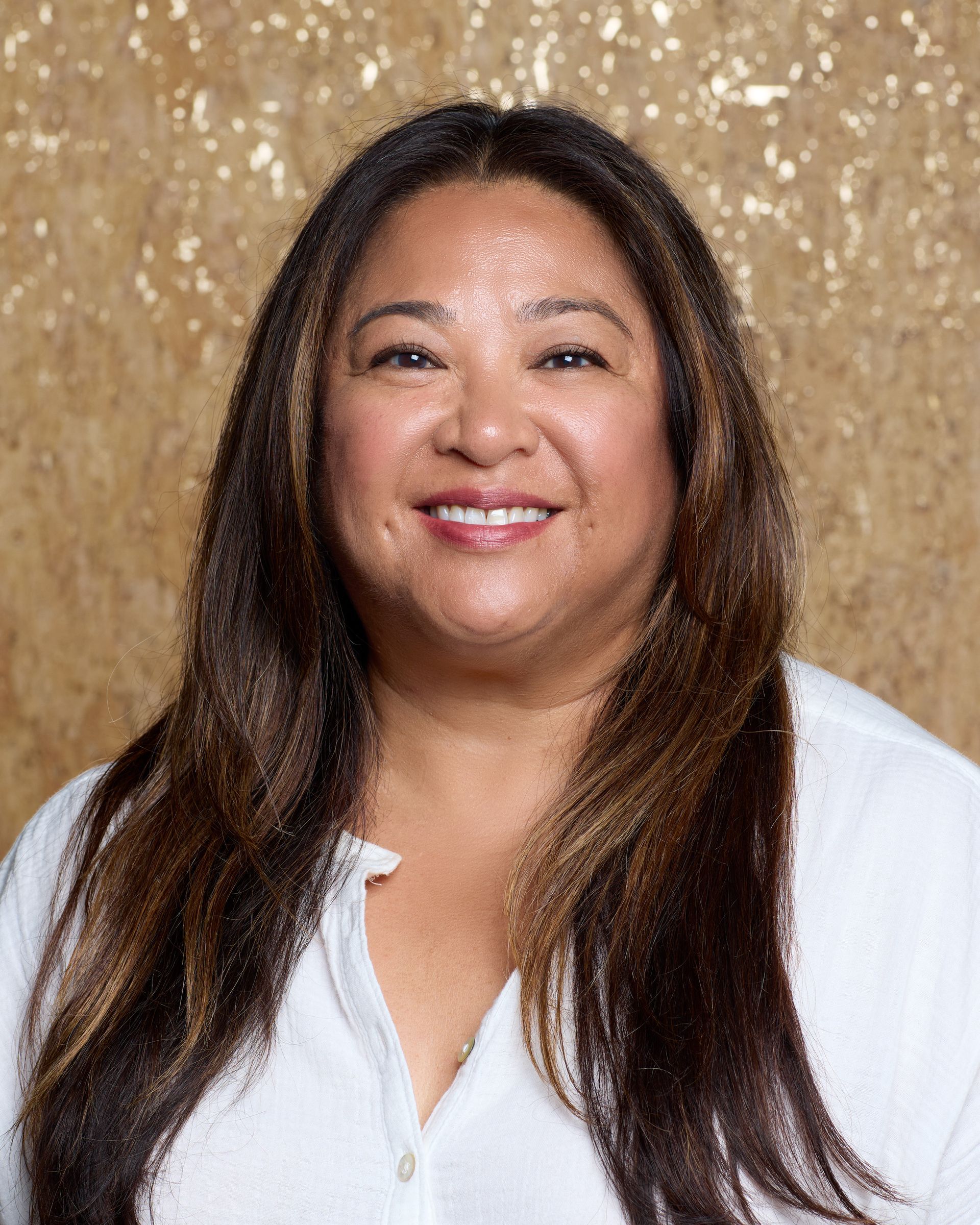 A woman with long hair is wearing a white shirt and smiling.