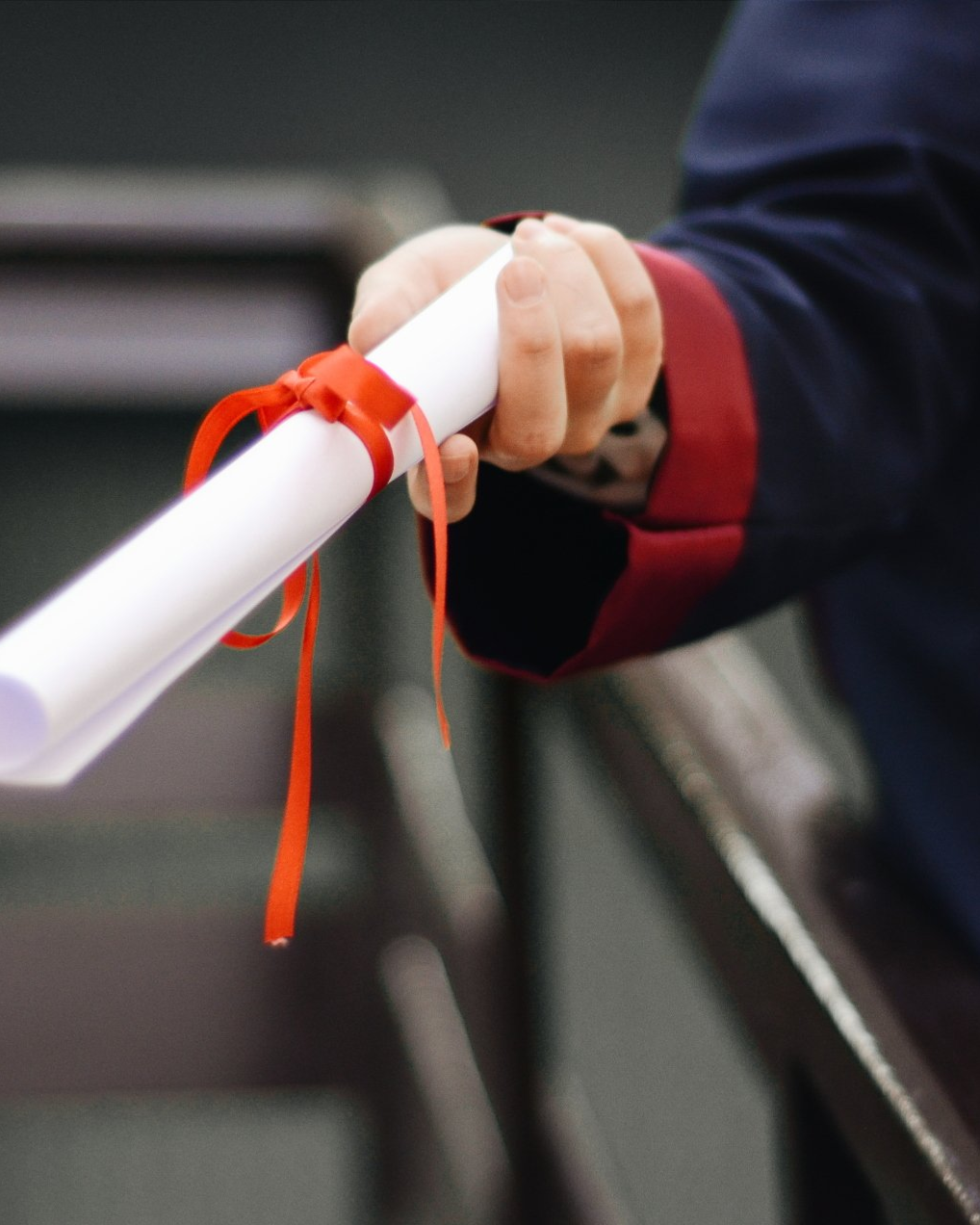 Hand holding a rolled diploma tied with a red ribbon
