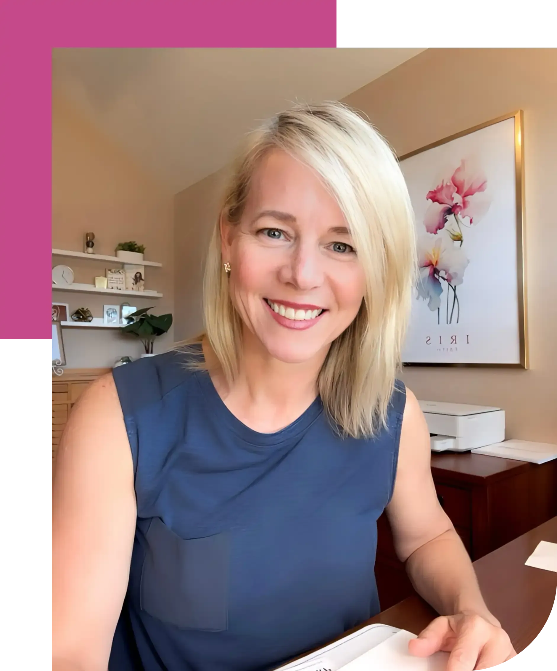 A woman is sitting at a desk in front of a painting of flowers.
