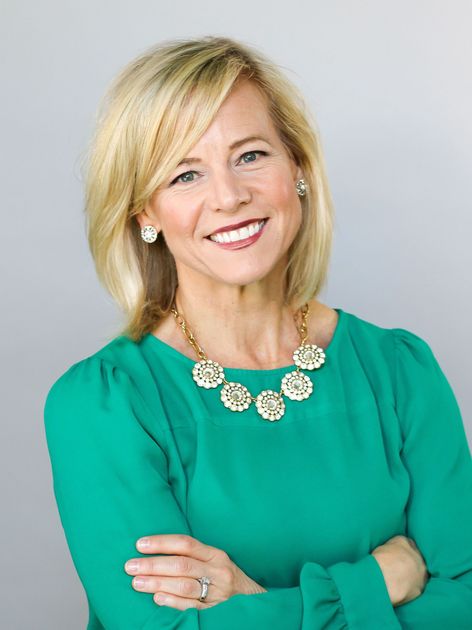 A woman in a green shirt and necklace is smiling with her arms crossed.