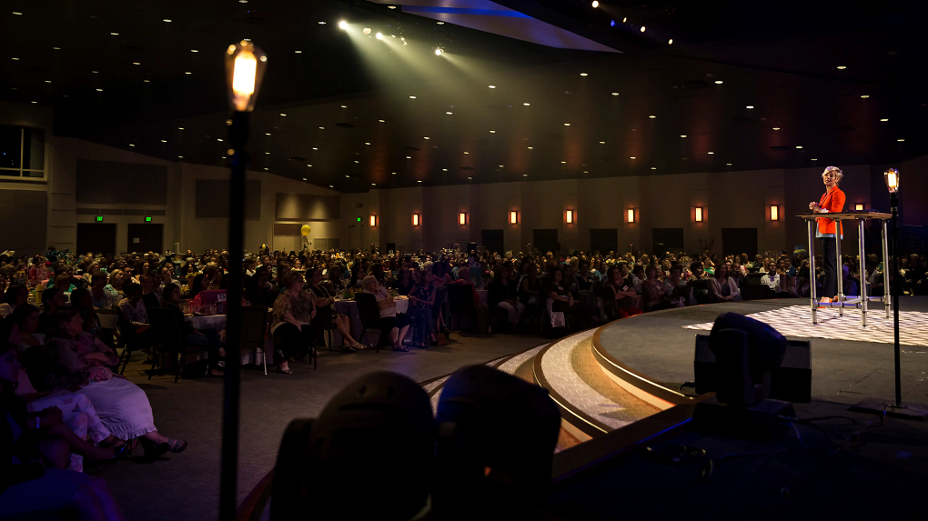 A woman is standing on a stage giving a speech to a crowd.