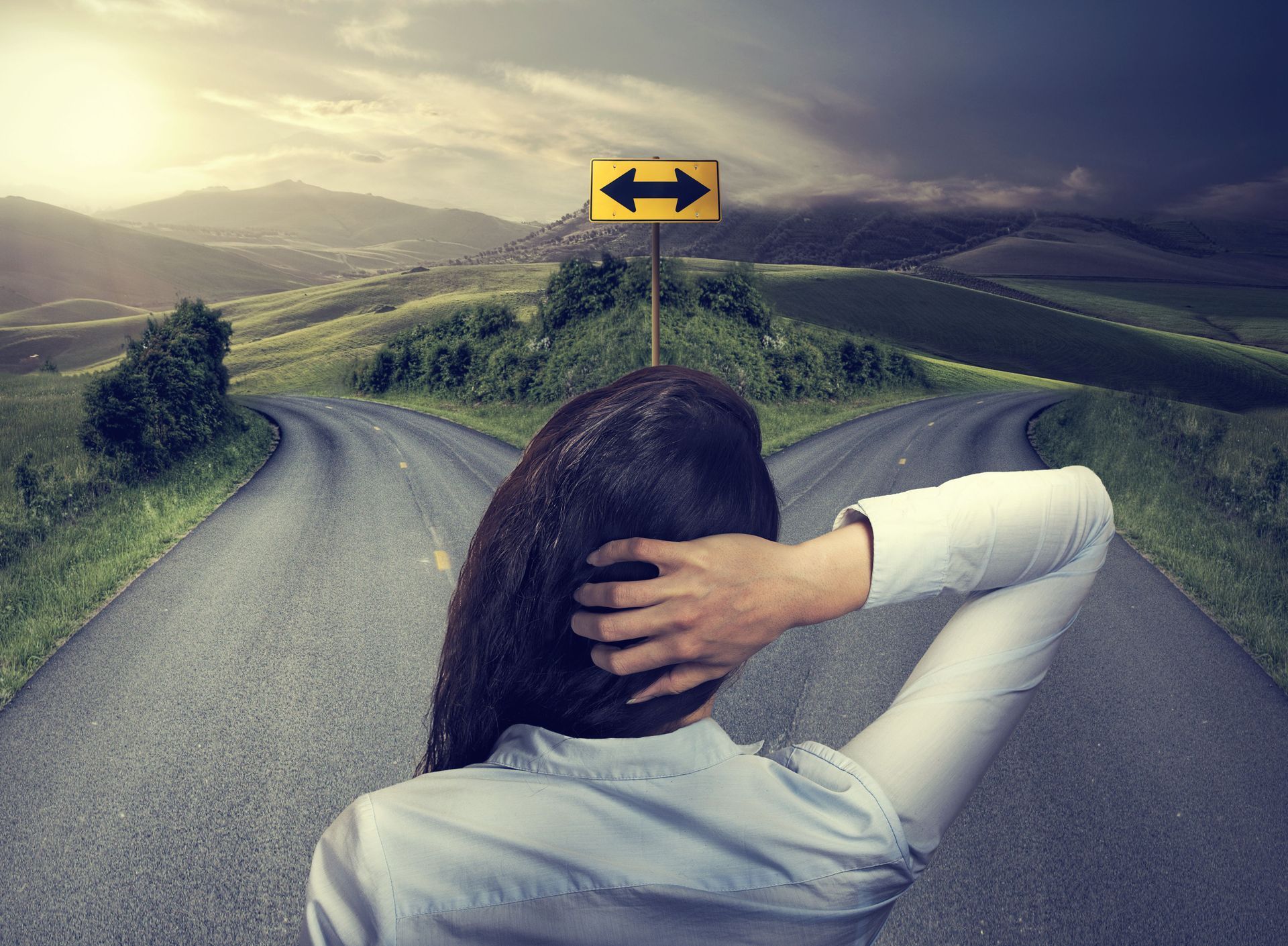 A woman is standing at a fork in the road looking at a sign.