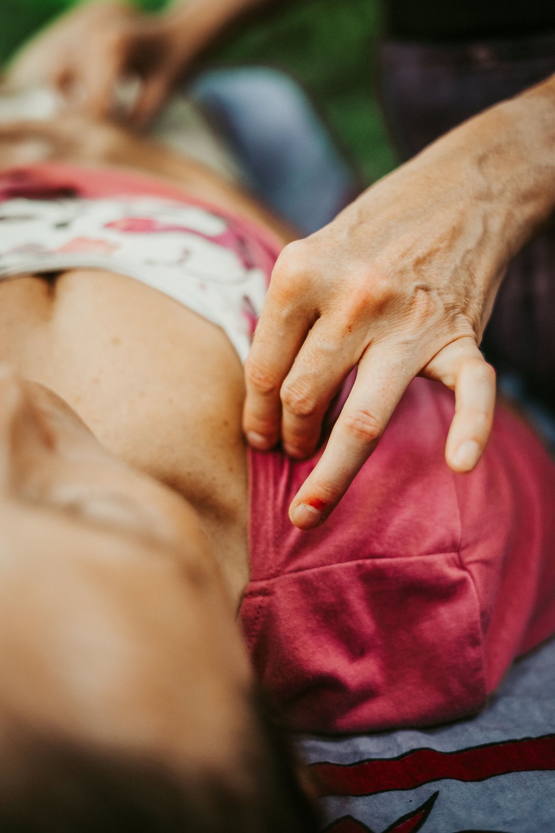 Person receiving massage, upper body detail. Hand presses on shoulder; red clothing and background.
