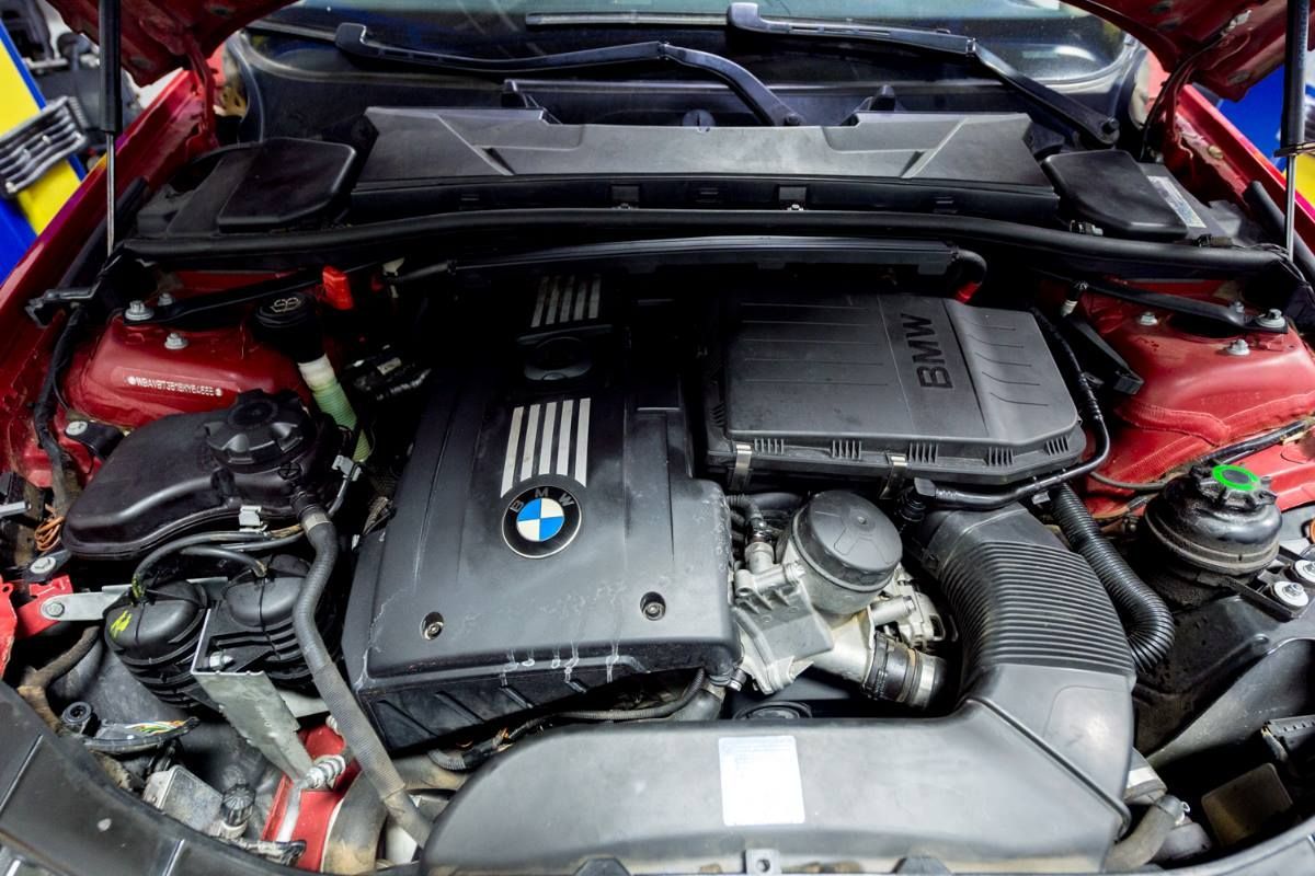 Red car engine bay with black engine cover bearing BMW logo.