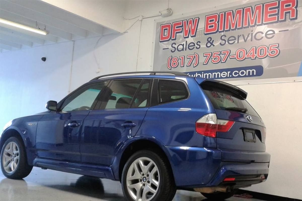 Blue BMW X3 SUV parked inside a dealership, with a sign for 
