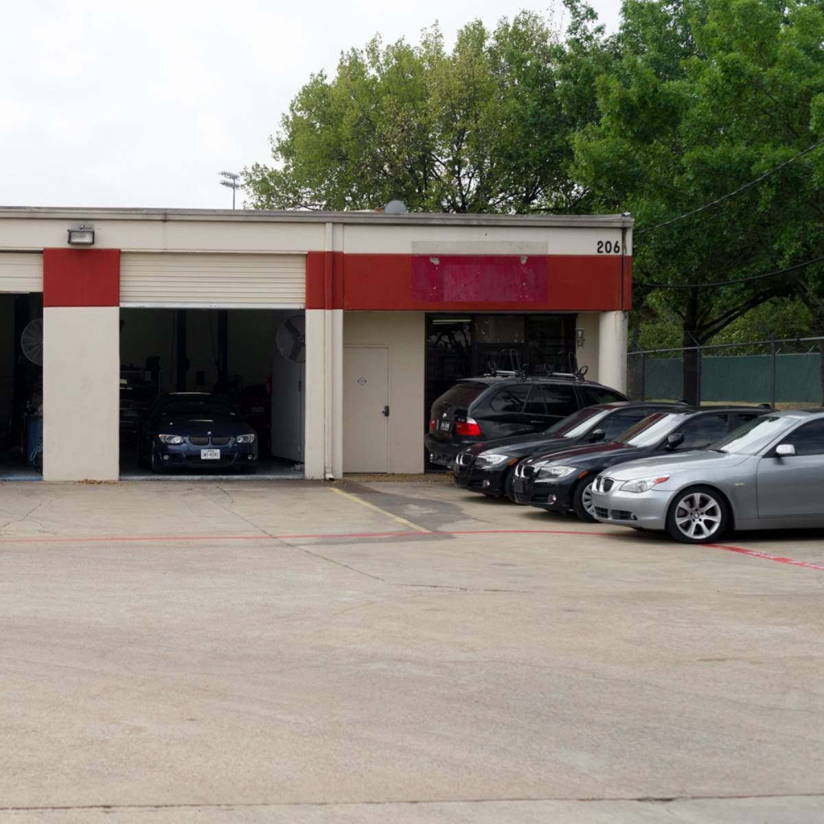 Exterior of a car repair shop with several cars parked in front of garage bays; red and white building.