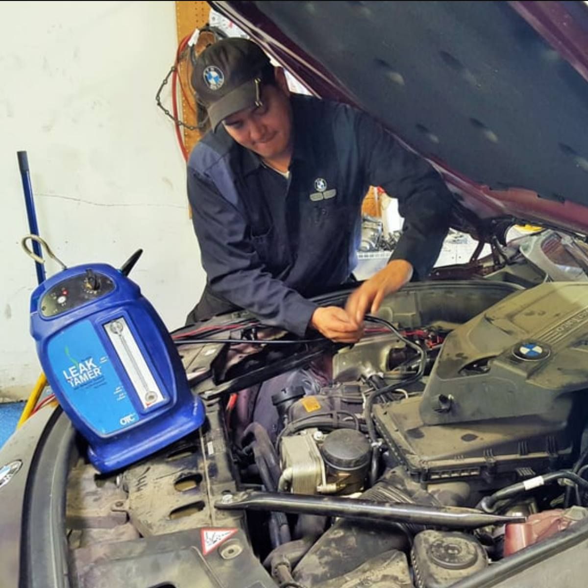 Mechanic working on a car engine with a blue leak detector in a garage.