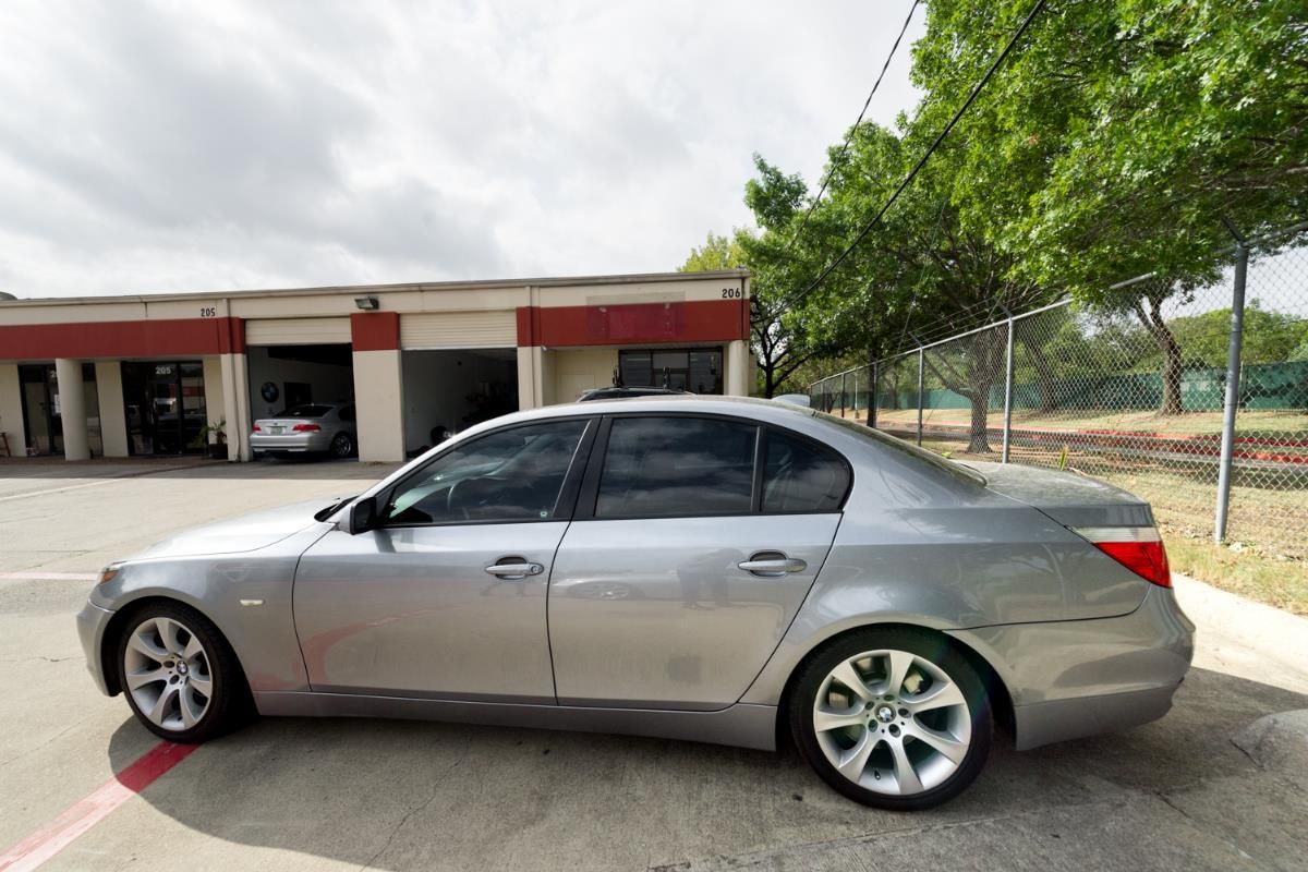 Silver BMW sedan parked outside a building with garage bays, overcast sky.