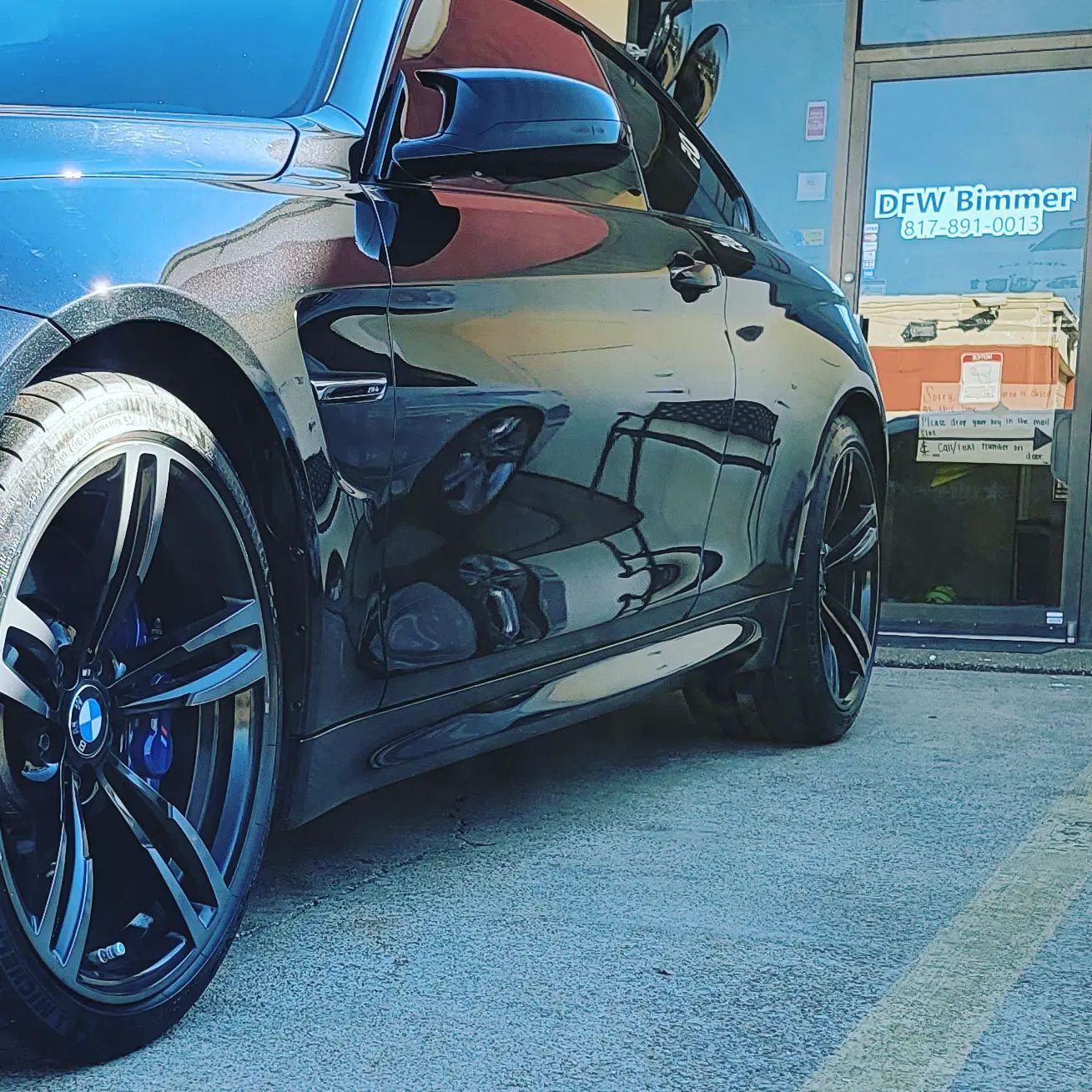Black BMW coupe with blue brake calipers, parked in front of a DFW BMW storefront.