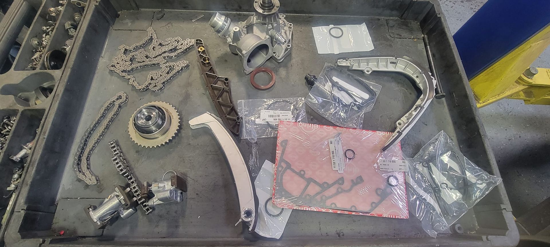 Various engine components on a tray, including chains, gears, and a water pump.