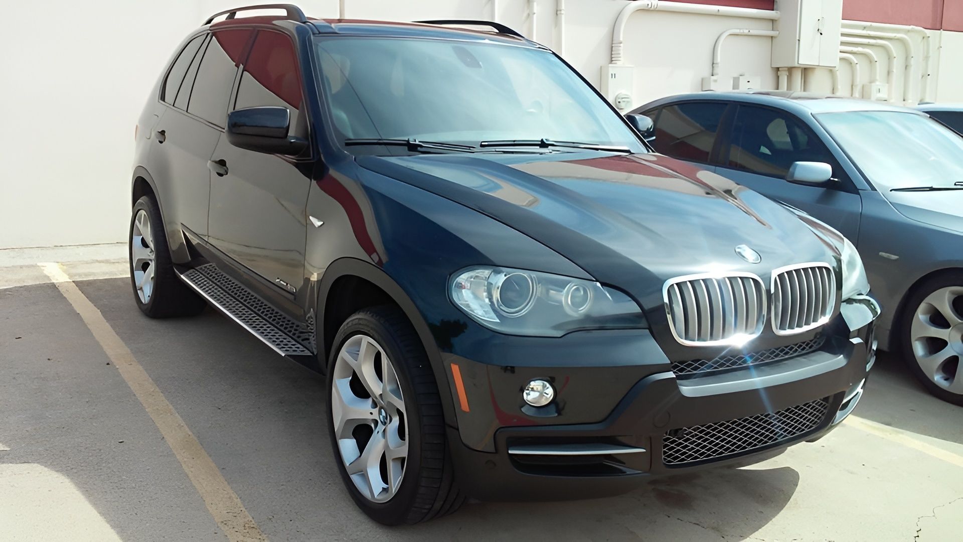 Black BMW X5 SUV parked in a parking lot, next to a silver car.