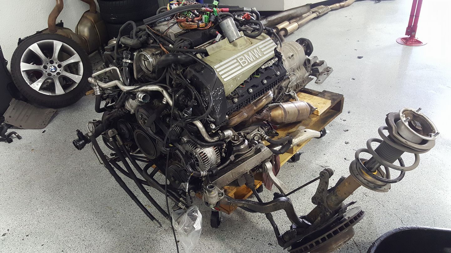 Disassembled car engine and front suspension components on a garage floor.