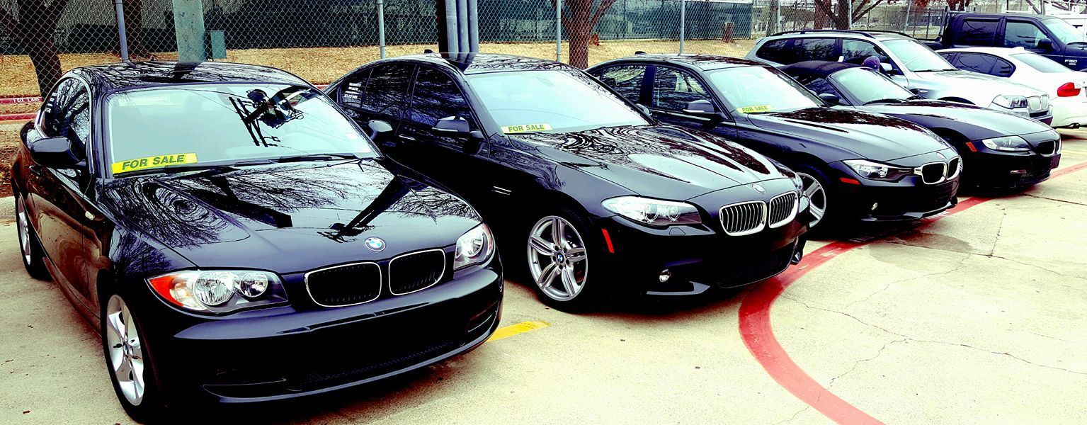 Several black BMW cars parked in a row on a concrete surface.