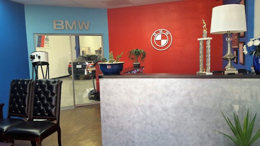 Reception area with BMW logo and waiting chairs; red, blue, and white wall colors.