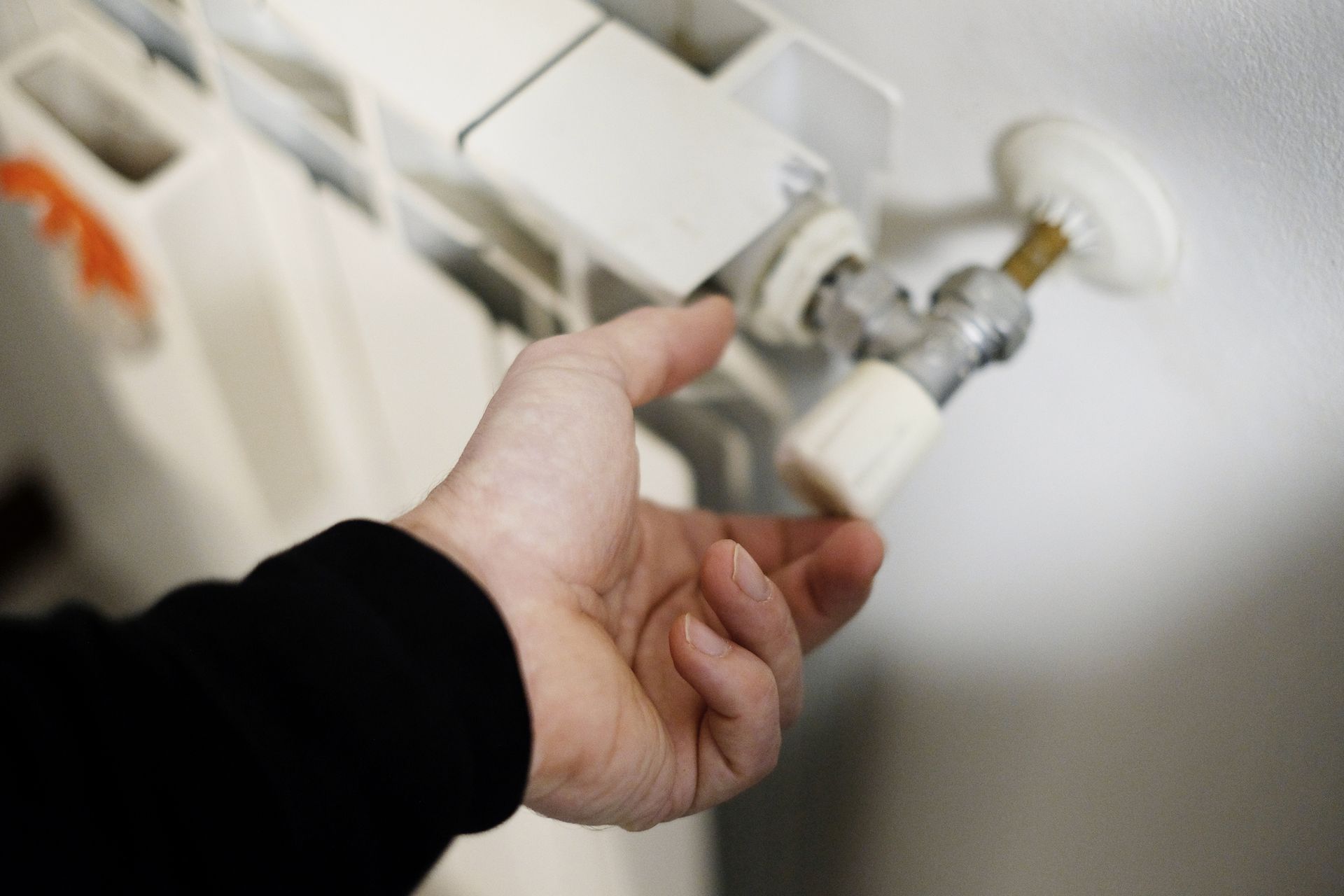 A person's hand turning a white valve on a radiator, likely adjusting the heat. The setting appears to be indoors. A person's hand turning a white valve on a radiator, likely adjusting the heat. The setting appears to be indoors.