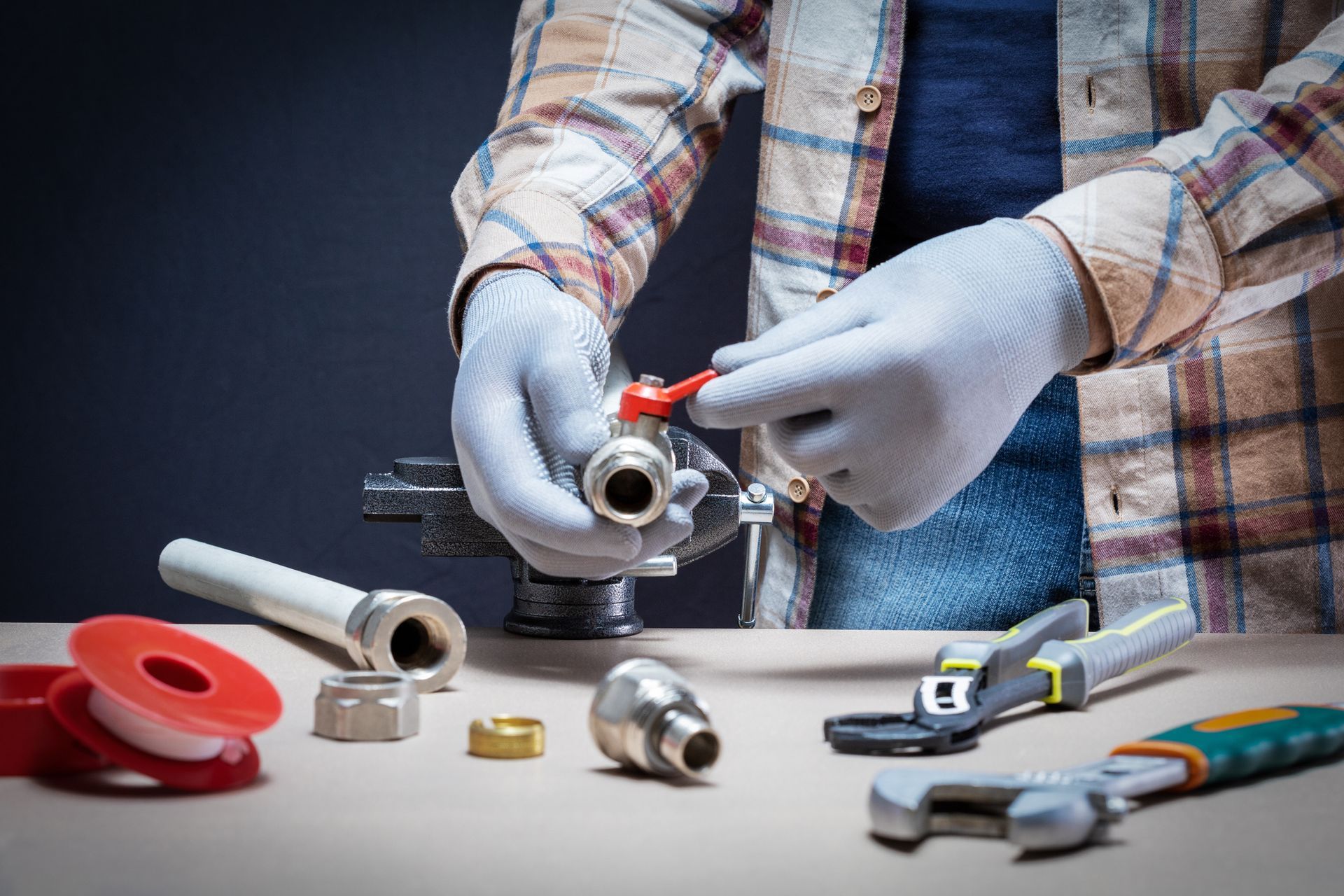 Plumber wearing gloves works on a valve with tools and parts on a wooden surface. Plumber wearing gloves works on a valve with tools and parts on a wooden surface.