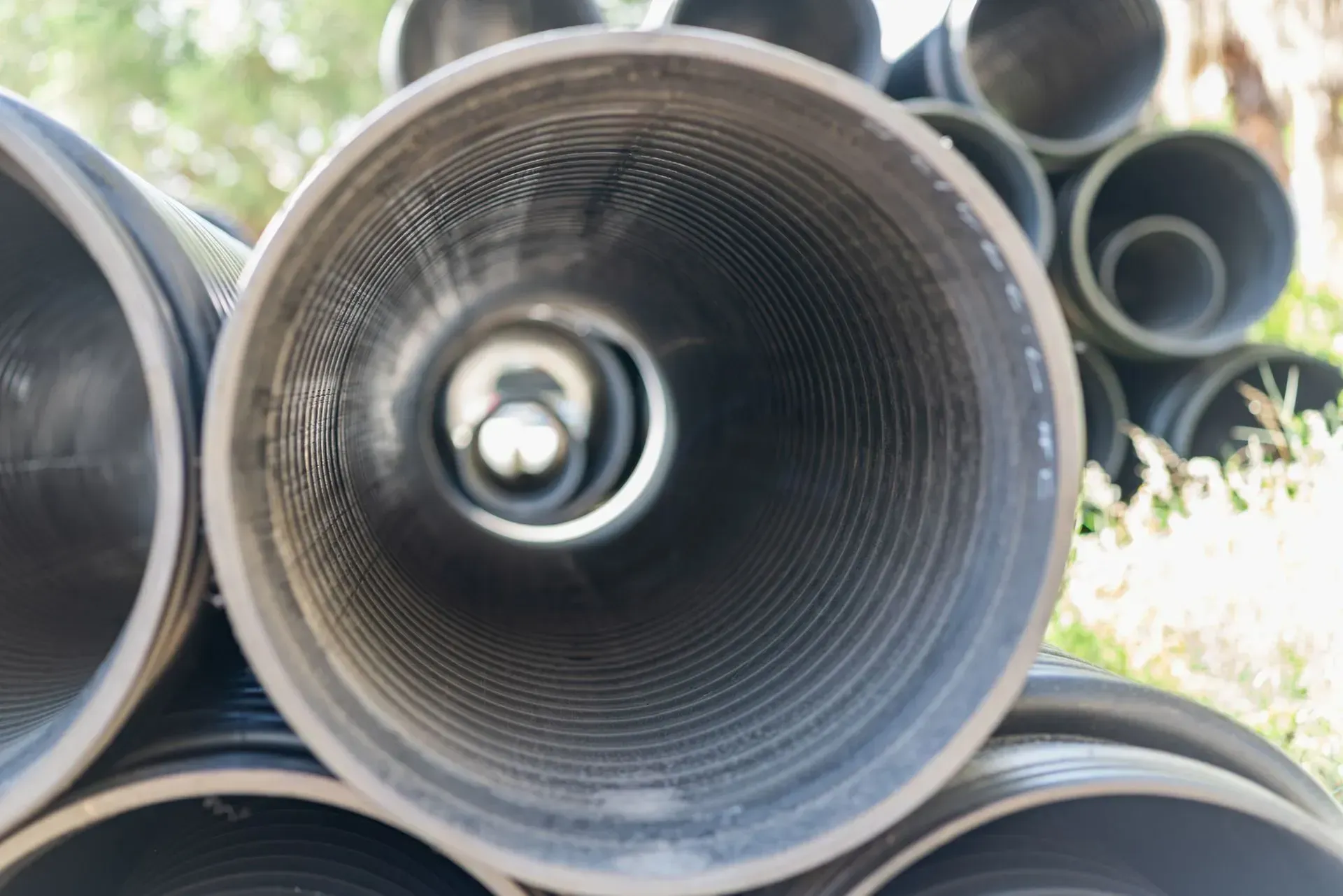 Stack of black corrugated pipes, viewed from inside one, showing concentric circles and a dim interior. Stack of black corrugated pipes, viewed from inside one, showing concentric circles and a dim interior.