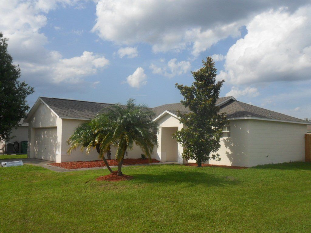 Blue sunny skies and a white house with a gray roof and two trees out front.
