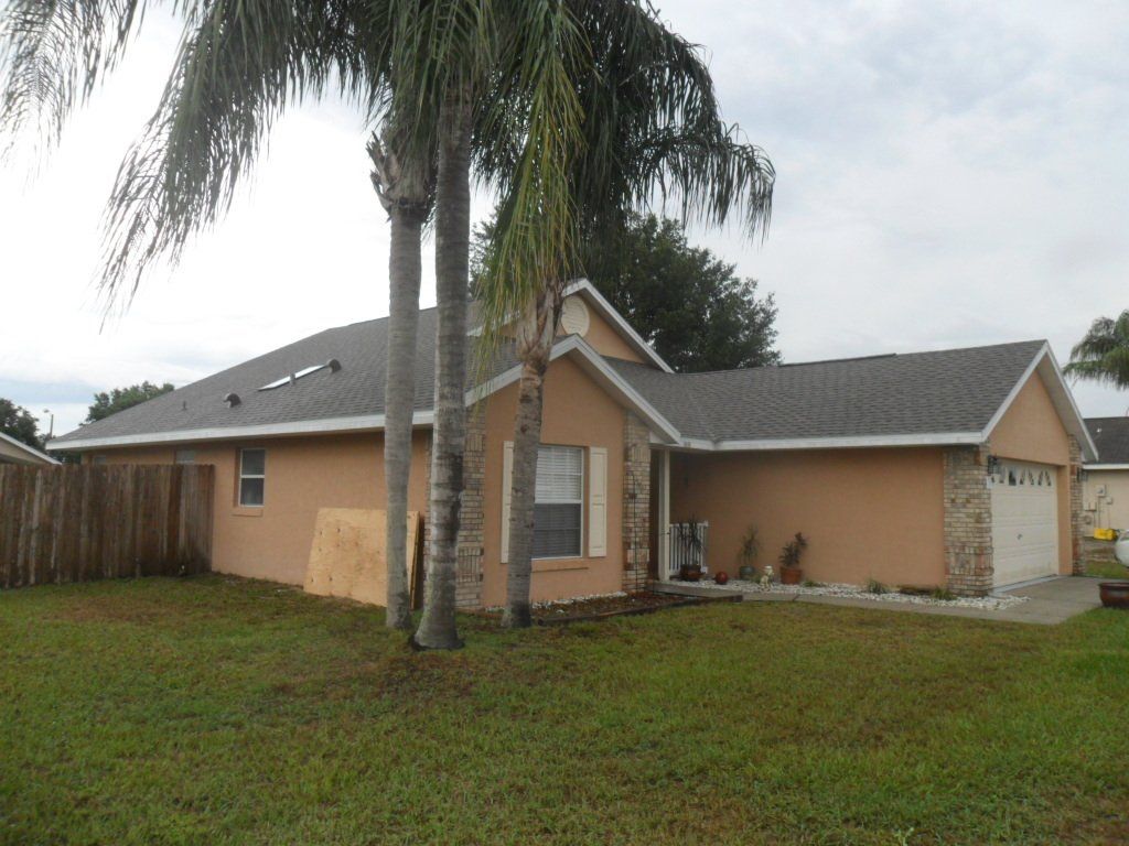 Tan house with a gray roof and wooden fence. Tall tree in front of the house.
