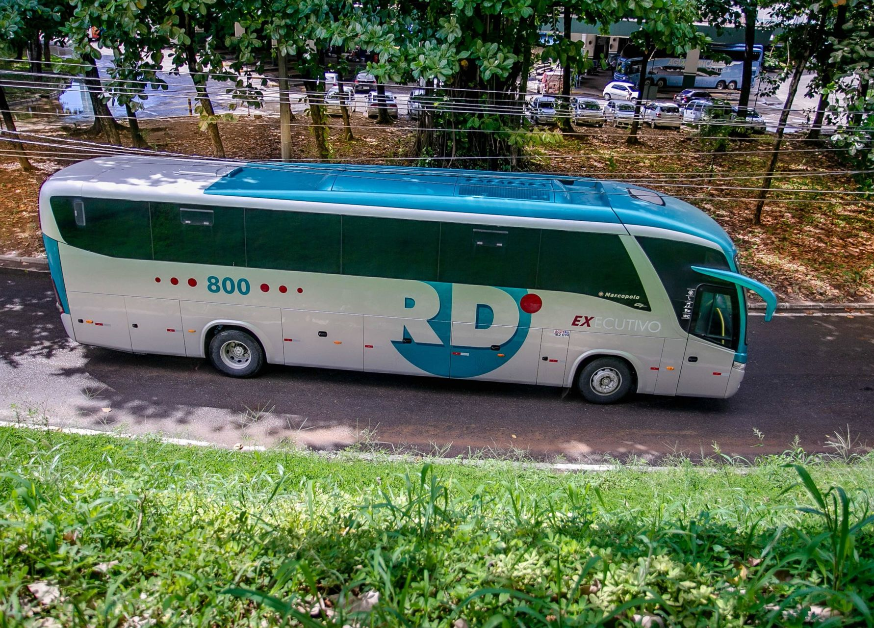Ônibus branco e verde com o logotipo da RD Transportes estacionado em uma rua arborizada