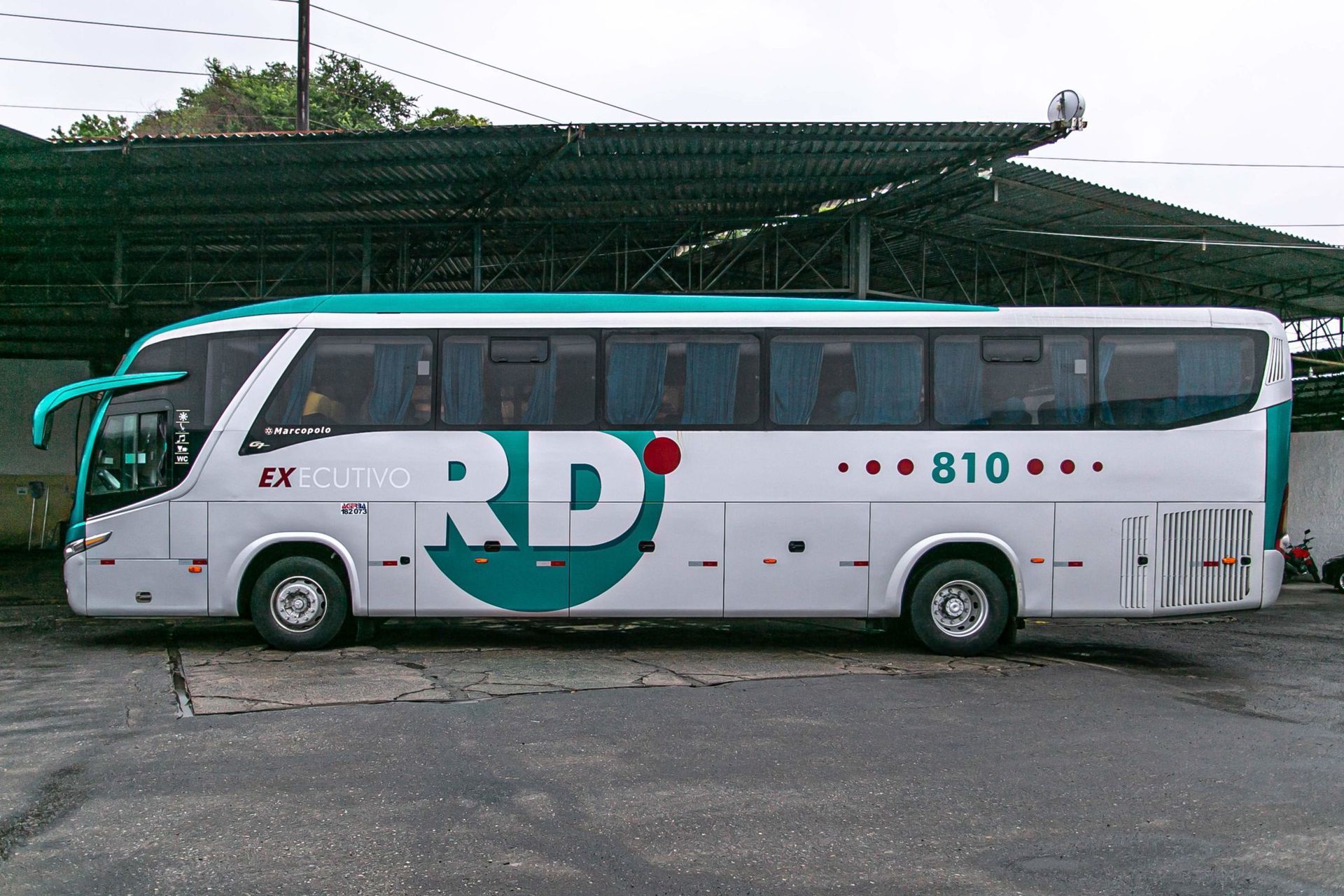 Ônibus branco e verde com o logotipo da RD Transportes na lateral estacionado em uma rua asfaltada