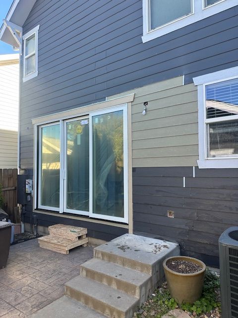 Back patio with sliding glass door, small concrete steps, and blue-gray house siding.