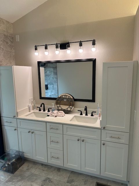 Bathroom vanity with large mirror, black light fixture, and light blue cabinets beneath a white countertop.