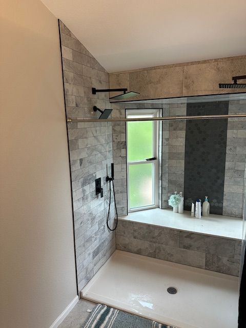 Modern tiled shower with glass partition, rain showerhead, built-in bench, and frosted window.
