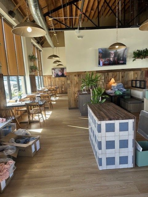 Bright restaurant interior with wooden tables, hanging lights, and a long central planter by large windows