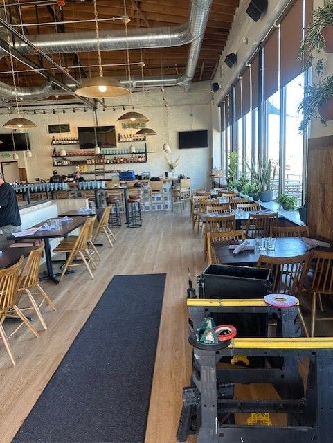 Spacious café interior with wooden tables, high ceiling, and large windows along the right side.
