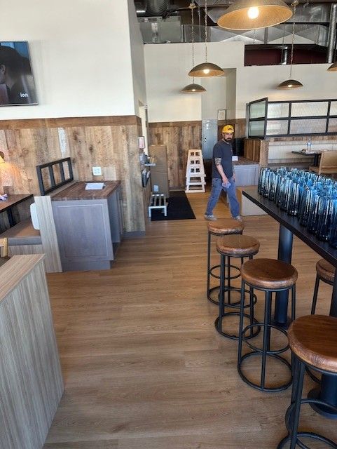 Modern restaurant interior with wooden tables, stools, and a person walking near the back.