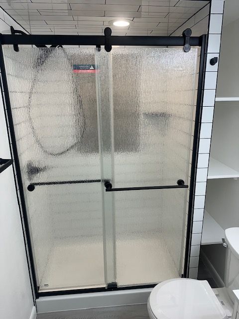 Frosted glass shower door with black frame in a tiled bathroom, with a white toilet visible on the right