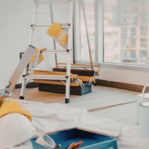 Painting tools and ladder in a room with a drop cloth, suggesting home renovation work