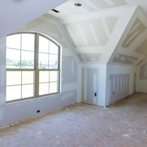 Empty unfinished room with sloped ceiling, arched window, and exposed drywall patches