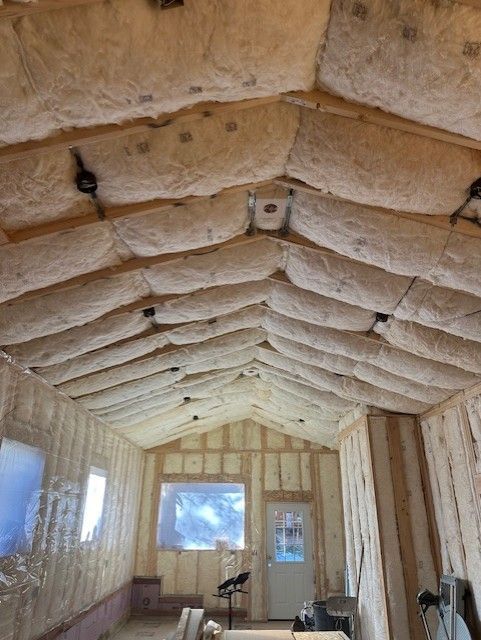 Interior of a small unfinished room with exposed insulation in the ceiling and walls, windows, and scattered tools.