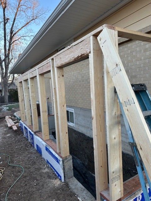 Partially built wooden porch frame along a house exterior with a ladder and blue sheathing below
