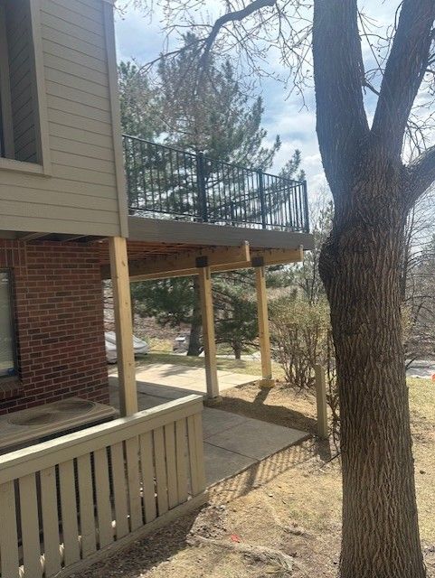 Side of a brick-and-beige house with a covered porch, trees, and a walkway in a yard.