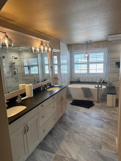 Bright bathroom with double vanity, large mirror, clawfoot tub, and window shutters.